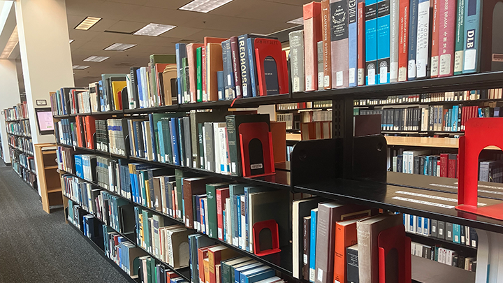 Rows of bookshelves filled with books in a library, with brightly colored bookends and overhead fluorescent lighting.